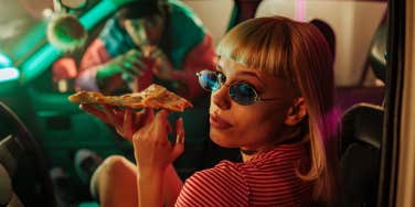 fashionable woman sitting in the car with pizza and her boyfriend looking through the passenger window