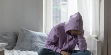 sad young person sitting on bed in hoodie