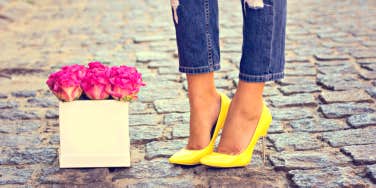 a woman's feet and lower legs, yellow high heels on cobblestones, next to pink roses
