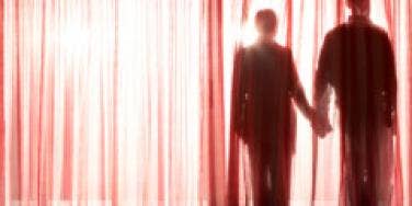 shadow of couple holding hands behind sheer red curtain