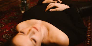 Woman laying on the floor of her bedroom with her ring on her chest contemplating her relationship