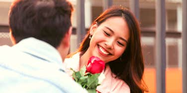 young Asian woman smiling as her boyfriend hands her a rose