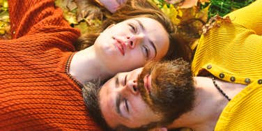 man and woman lying in autumn leaves looking up at sky together