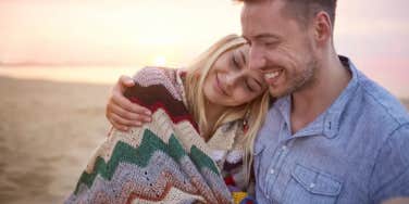 Woman smiling laying on man's shoulder as the sun sets