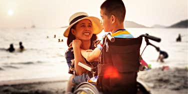 mom and son who uses wheelchair looking lovingly at one another on beach