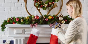 woman filling christmas stockings over fireplace