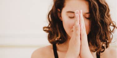 woman with full, curly hair has eyes closed and hands in prayer 