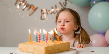 little girl blowing out candles on birthday cake in front of decorations