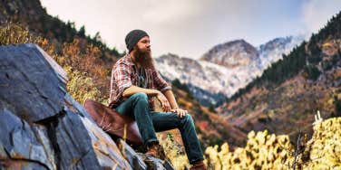 Bearded man sitting in the mountains on a rock