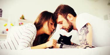 couple in a white bed snuggling their black cat