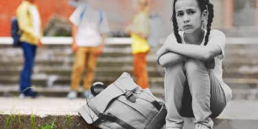 Little girl sitting on the steps of her school, with her backpack