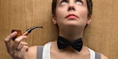 woman wearing a bowtie looking up while holding a pipe