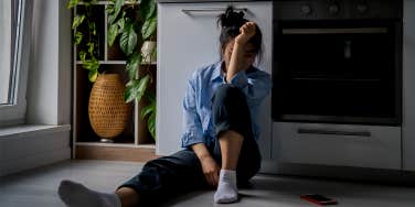 Woman sitting on kitchen floor with her face covered by her arm