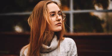 young strawberry blonde woman with round wire-rimmed glasses, looking away thoughtfully 