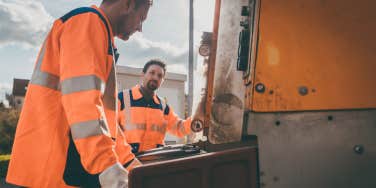 Garbage removal men working for a public utility emptying trash container