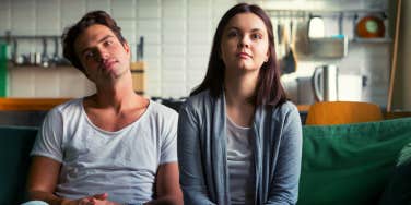 Lazy millennial couple getting bored at home sitting on sofa