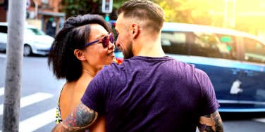 man with back to camera embracing woman wearing sunglasses and smiling