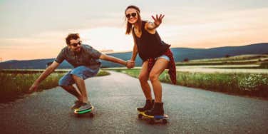 man and woman holding hands while skateboarding