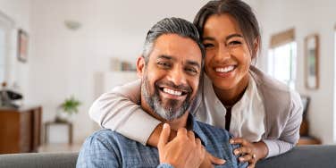 couple embracing and looking at camera sitting on sofa.