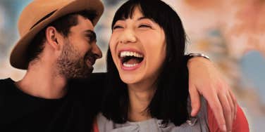 man whispering in woman's ear as she smiles