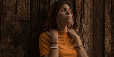 Woman in Orange Turtleneck Shirt Leaning on Brown Wooden Wall