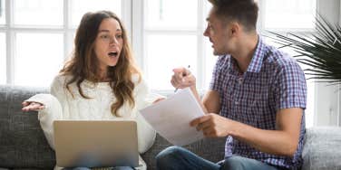 unhappy couple arguing while sitting on couch in front of laptop and papers
