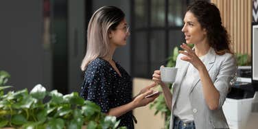 Two young business women chatting during work break standing in modern office