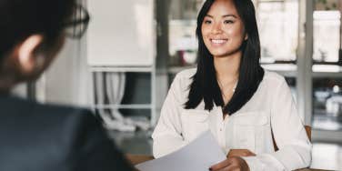 woman smiling and holding resume while sitting in front of businesswoman during corporate meeting or job interview