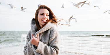 joyful woman on a beach with birds flying behind her