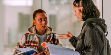 two high school girls looking at notebooks in hallway