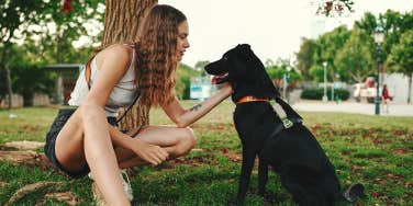 woman petting black dog outside in park