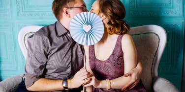 couple kissing behind fan with blue heart