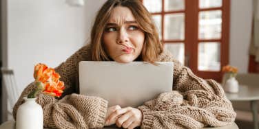 woman in sweater with computer looking uncertain