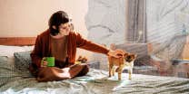 Introvert woman drinking coffee and petting her cat on her bed 