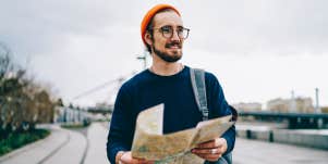 smiling male traveler walking with map having city tour excited with urban setting on autumn weekends