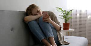 Woman sadly uses on her phone while alone on a couch