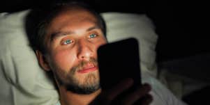man looking at phone while laying in bed