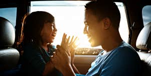 Asian father playing with his daughter in a car, boy laughing, backlit