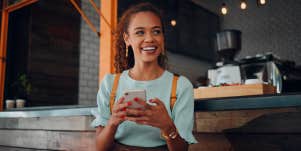 happy woman sitting at coffee shop holding phone