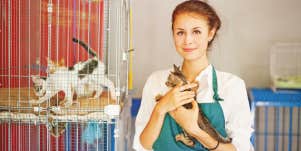 animal shelter working holding cats next to kennel of cats