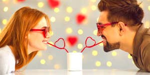 woman and man wearing heart glasses and sharing a drink through straws