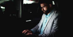 guy typing on laptop doing work at night in back of car