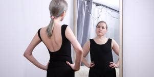 skinny woman looking in mirror at larger version of herself