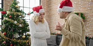 couple in santa hats arguing in front of christmas tree