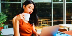 woman sitting drinking coffee while working on laptop