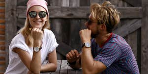 Couple sitting at a picnic table, him looking at her, she is smiling