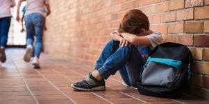 upset kid sitting against wall with his backpack