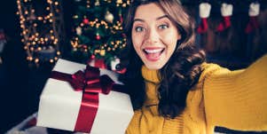 woman taking selfie for Instagram in front Christmas tree holding a present