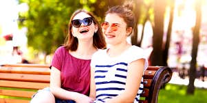 Two women sit on a park bench and laugh