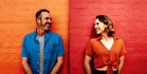 couple standing in front of an orange and red wall, looking at one another